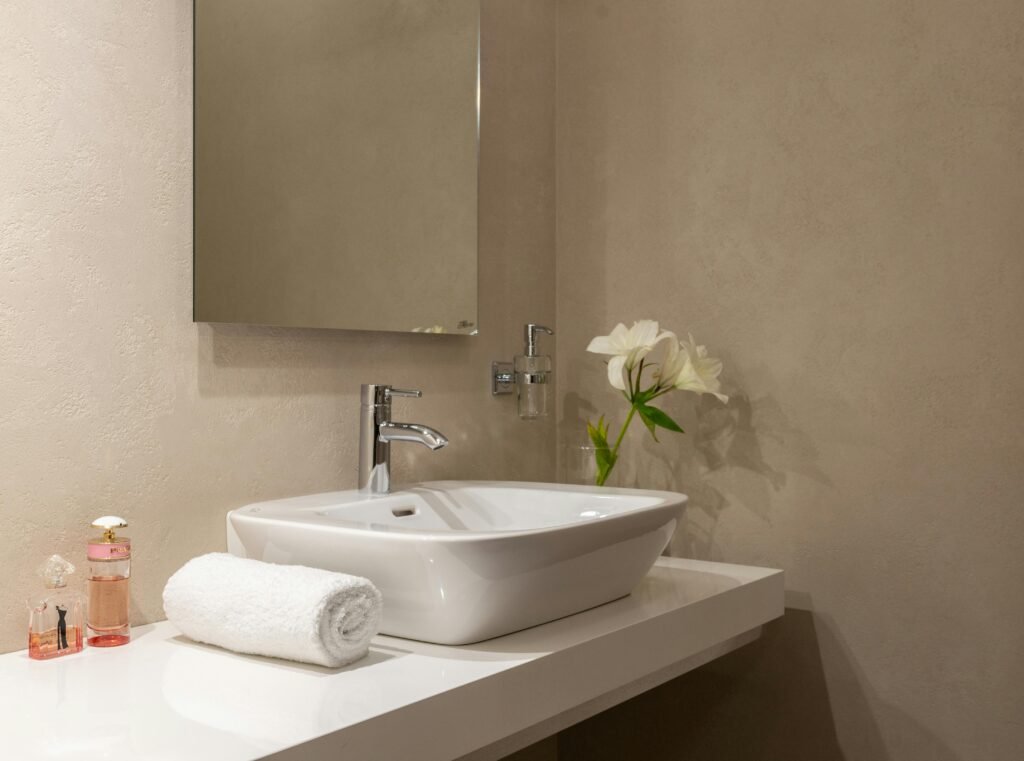 Interior of bathroom with white wrapped towel near ceramic basin and faucet with mirror on wall